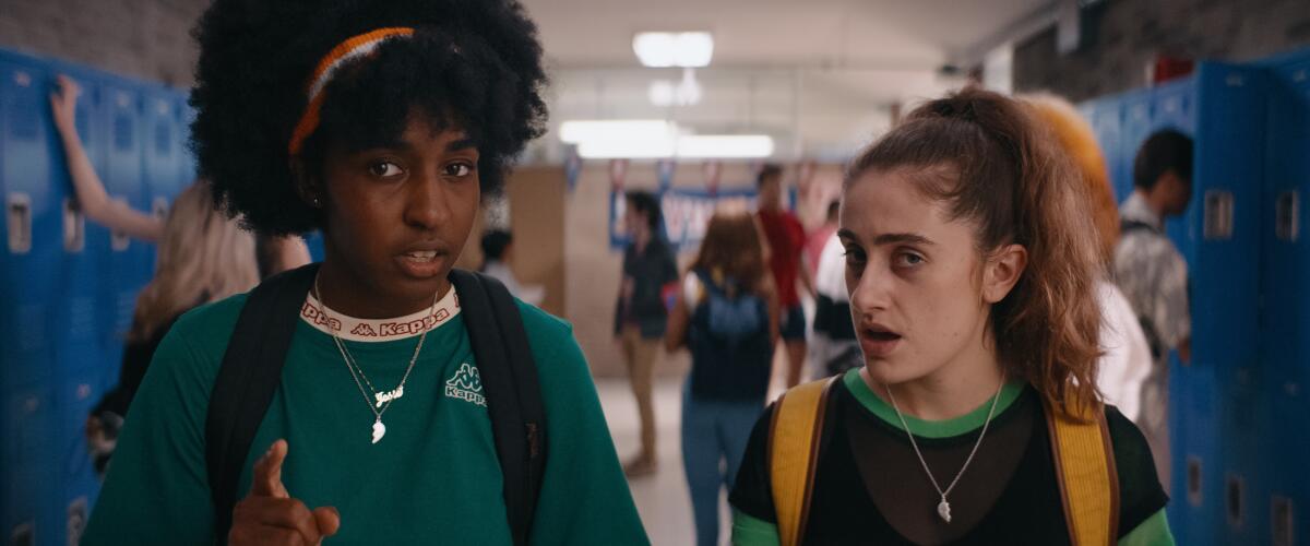 Two women speak to an off-frame person in a high-school hallway.