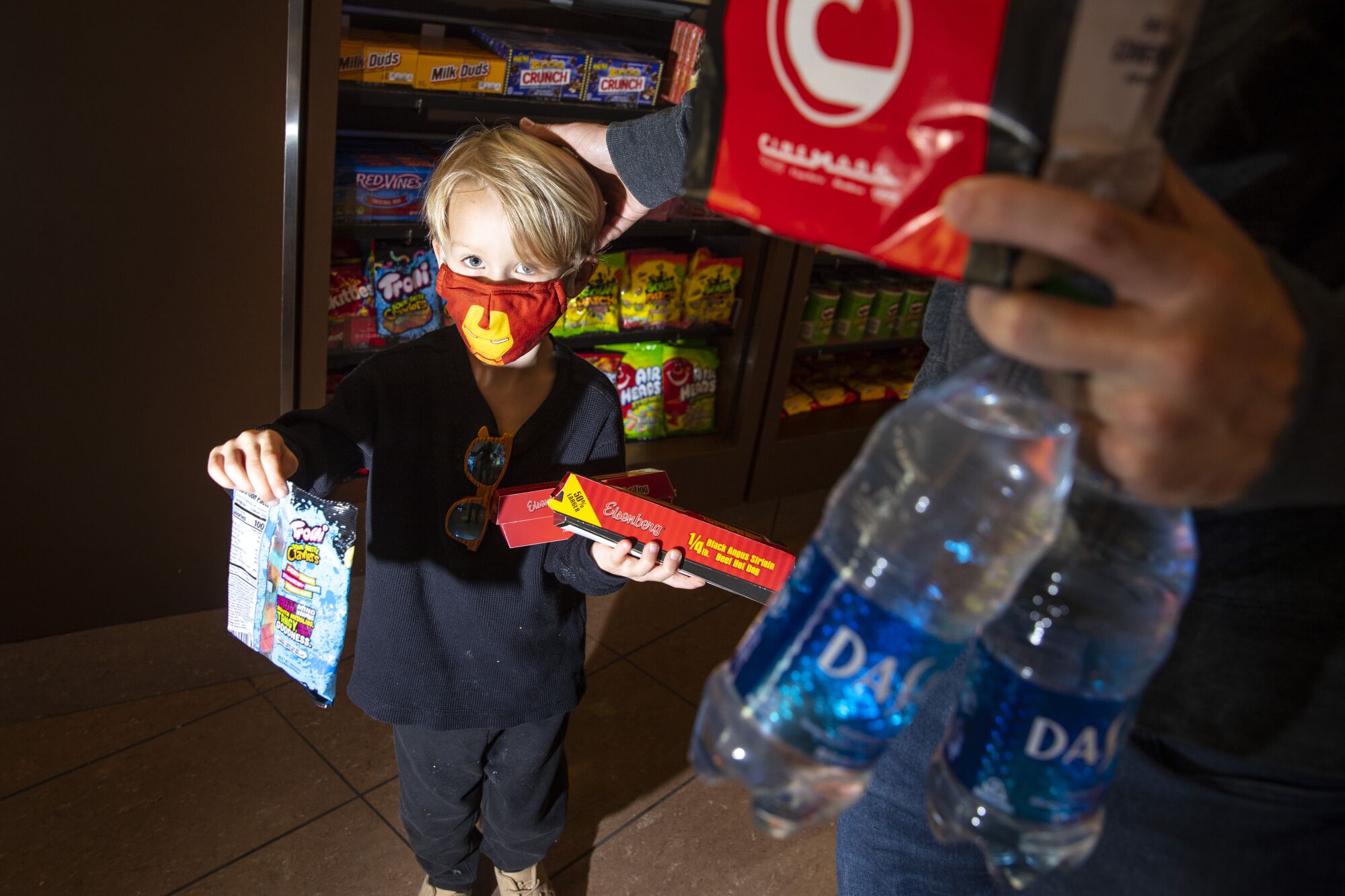 A masked child holds movie theater treats 