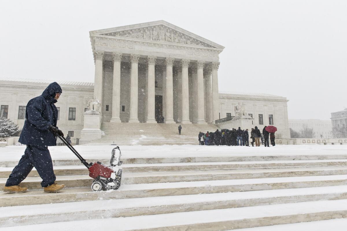 A worker clears snow from the plaza at the Supreme Court in Washington on Monday as those waiting to hear oral arguments line up.