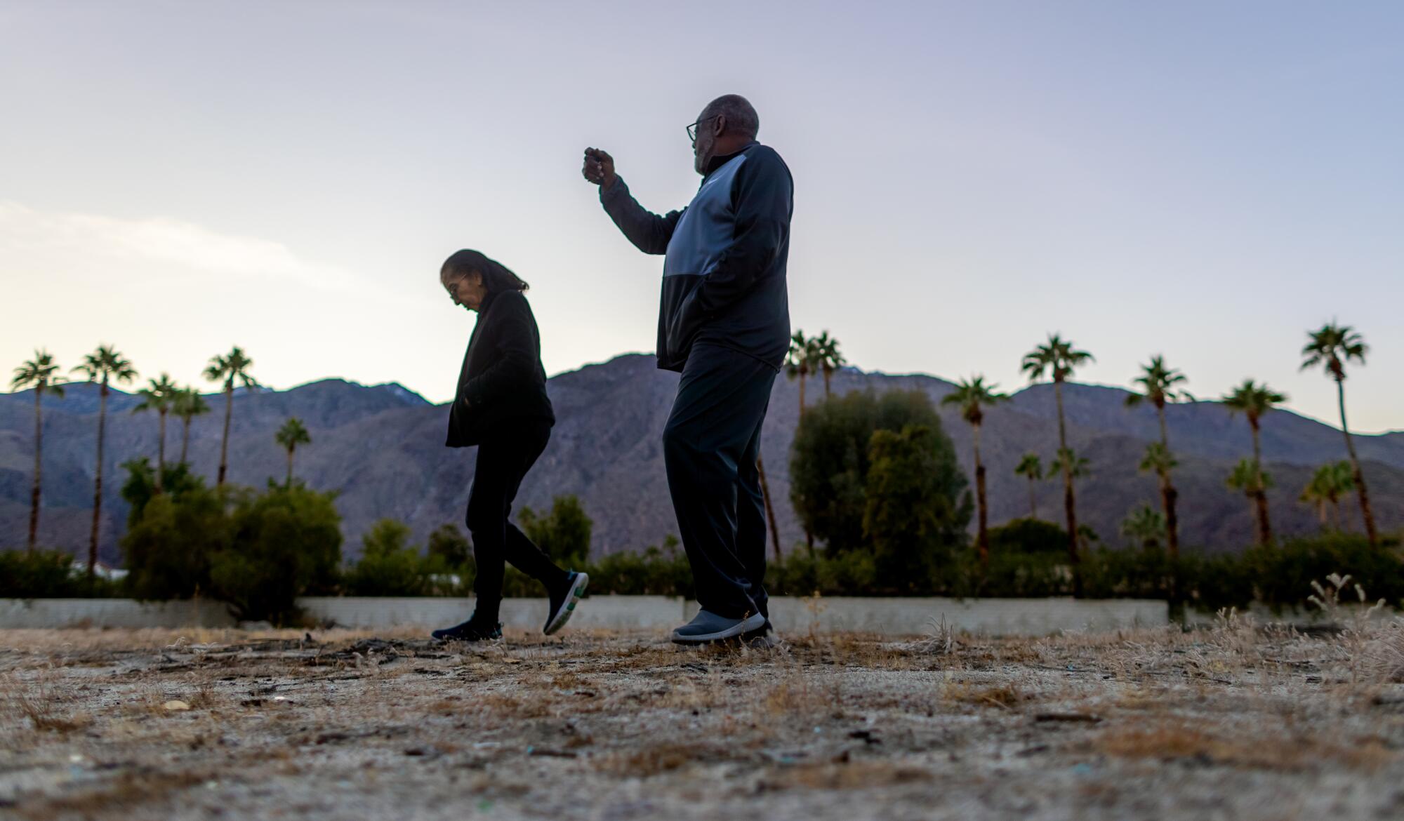 Two people walk on a vacant lot.