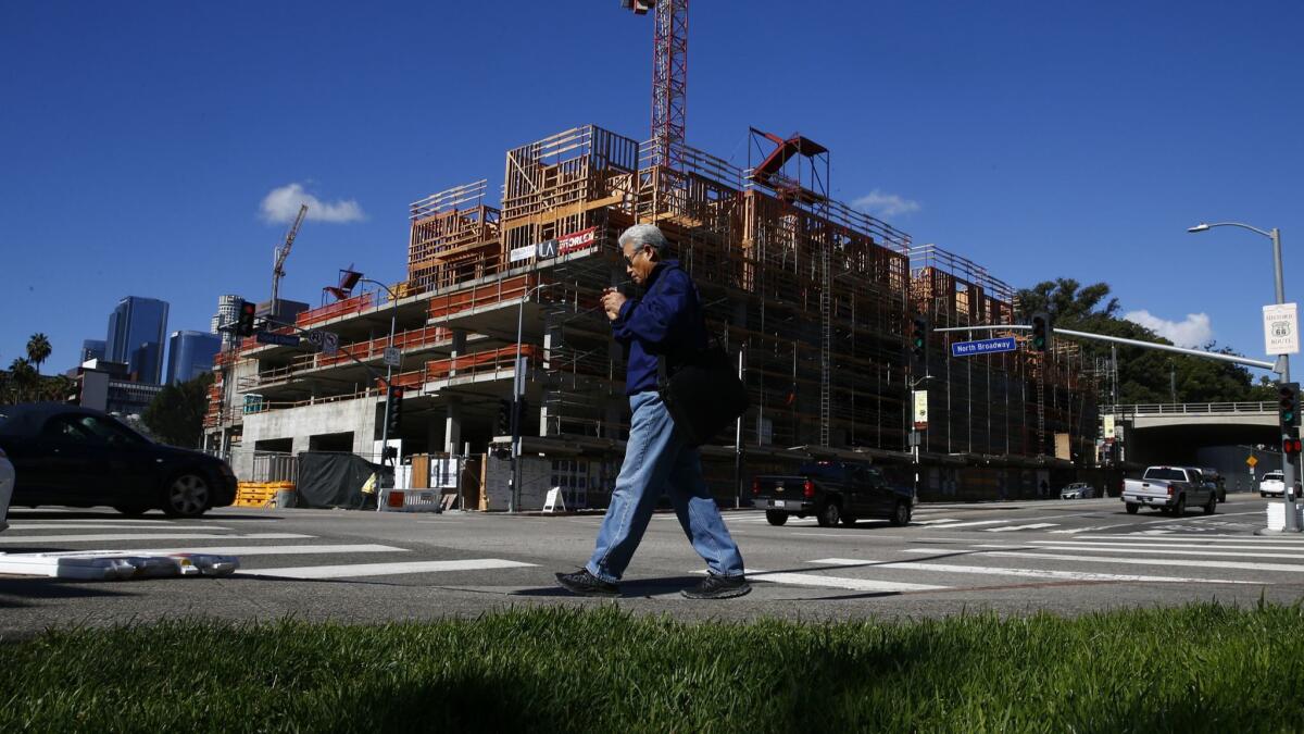 A man walks near a residential project going up at the corner of Cesar Chavez and Broadway near Chinatown in Los Angeles.
