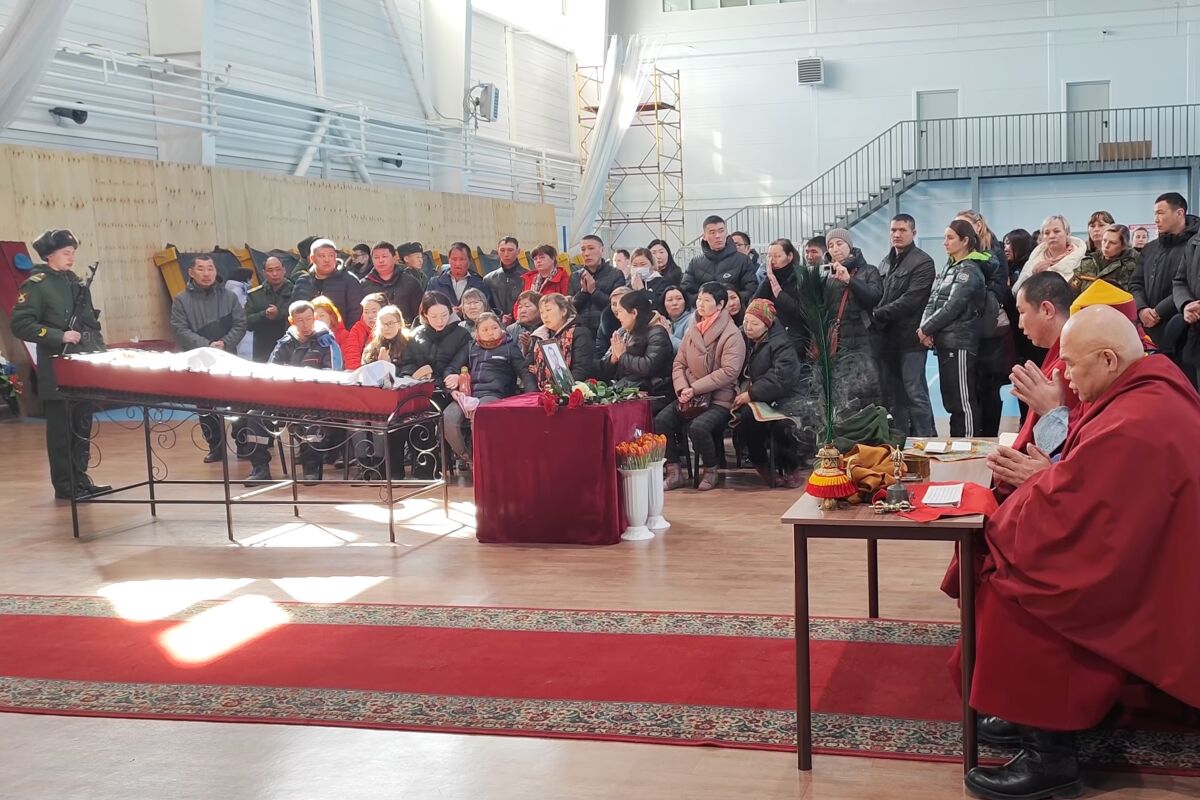 People stand and sit near two monks at a table.