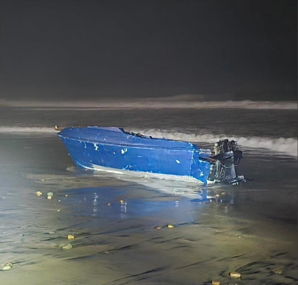 A blue boat in shallow water at night.