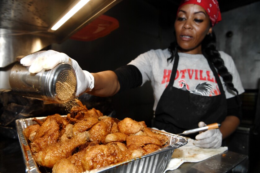 Kim Prince shakes spices onto a tray of hot chicken.