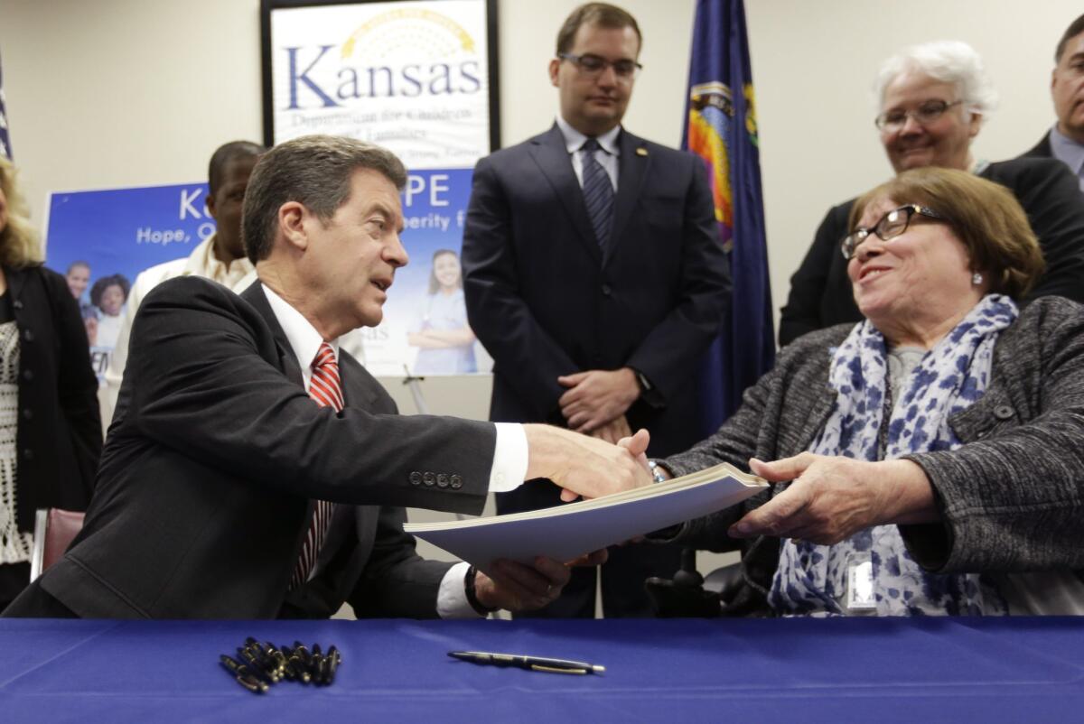 Gov. Sam Brownback, left, shakes hands with Phyllis Gilmore of the Department for Children and Families after signing a welfare-reform bill into law Thursday. The law restricts what welfare recipients can use their government funds for, including alcohol and tattoos.