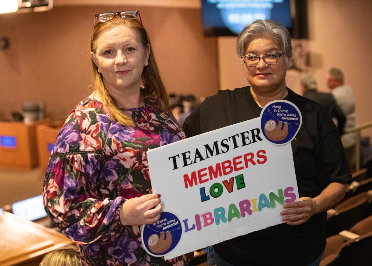 Gretchen Erickson and Bev Campos hold a sign in support of public libraries during Tuesday's meeting.
