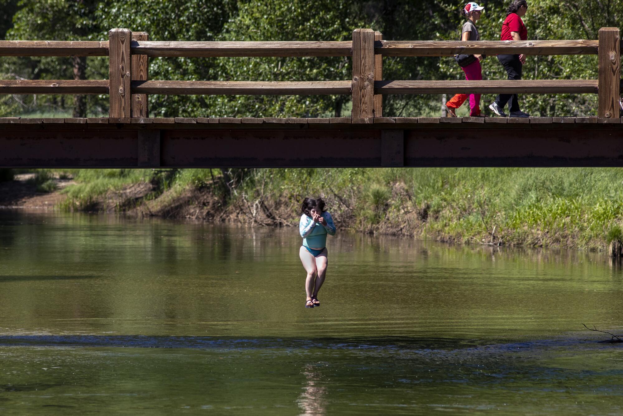 A young woman jumps off Swinging Bridge into the frigid Merced River.