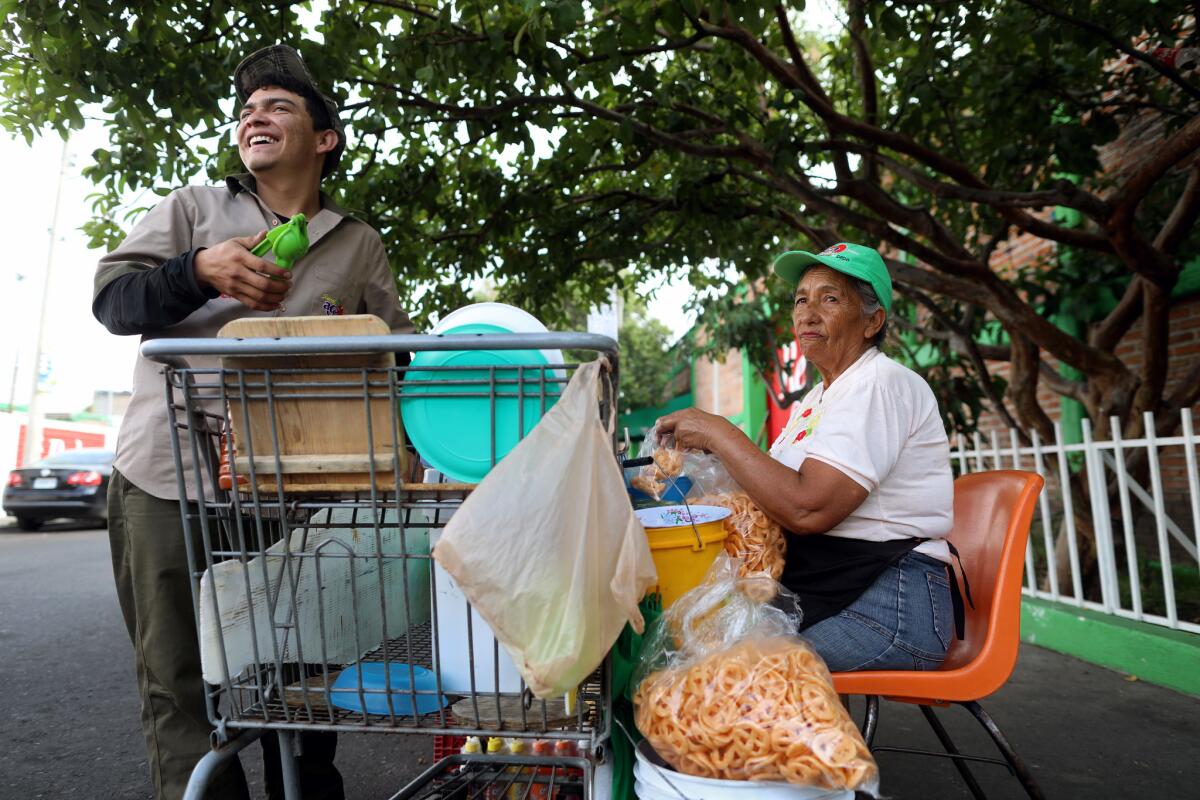 Maria Concepcion Arias Cazola, right, a member of La Luz del Mundo Church, makes on average $300 pesos ($16 U.S.) a day selling snacks in front of a soft drink distributor warehouse in the Hermosa Provincia neighborhood. (Gary Coronado / Los Angeles Times)