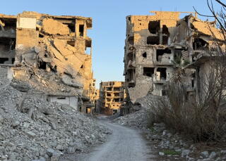 A path flanked by exposed, damaged multistory buildings and lined with rubble