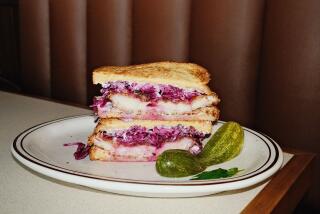 Two stacked halves of a chicken schnitzel sandwich filled with purple cabbage on a plate with a pickle at Belle's