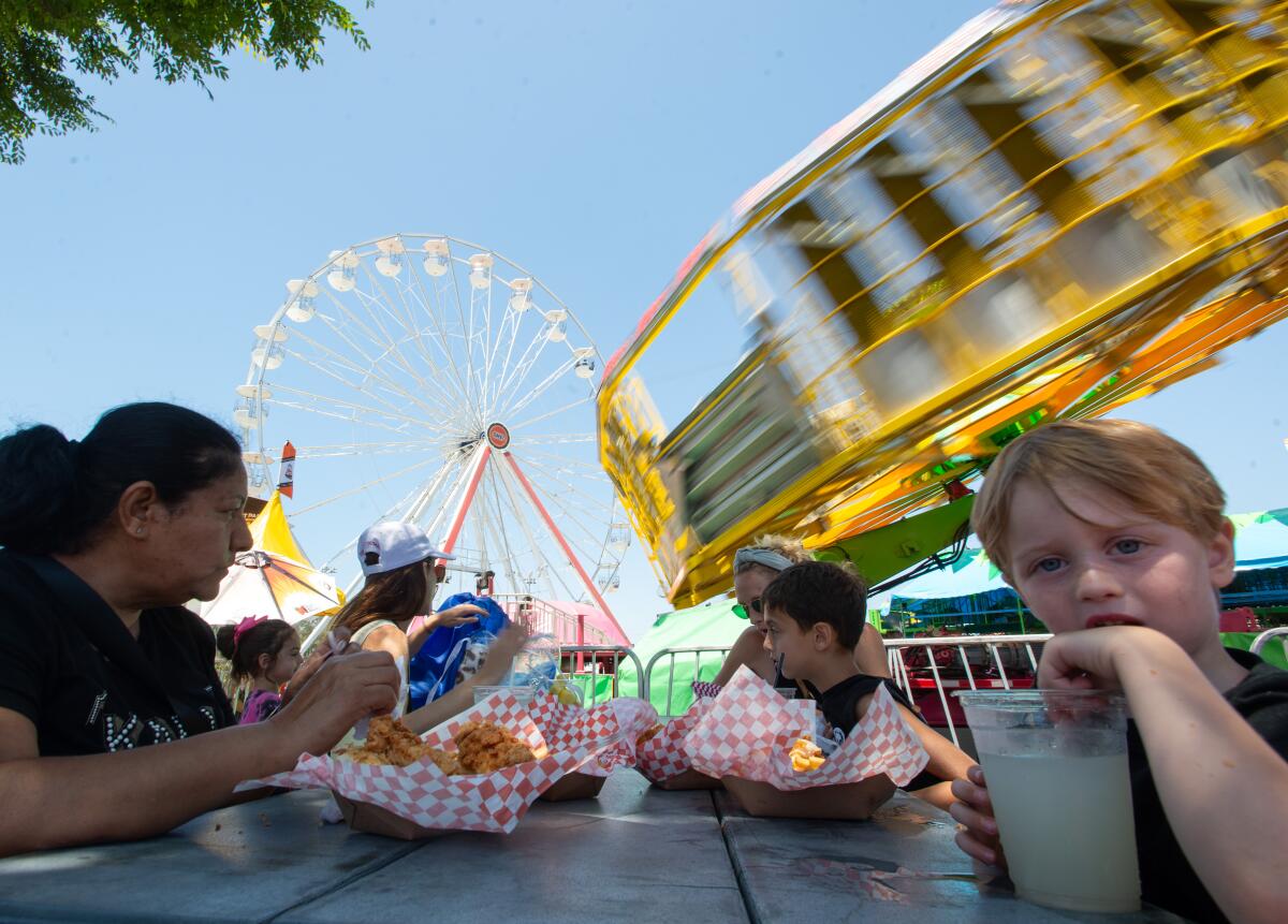 A family chows down on fried chicken strips and lemonade while a Ferris wheel and another ride spin.