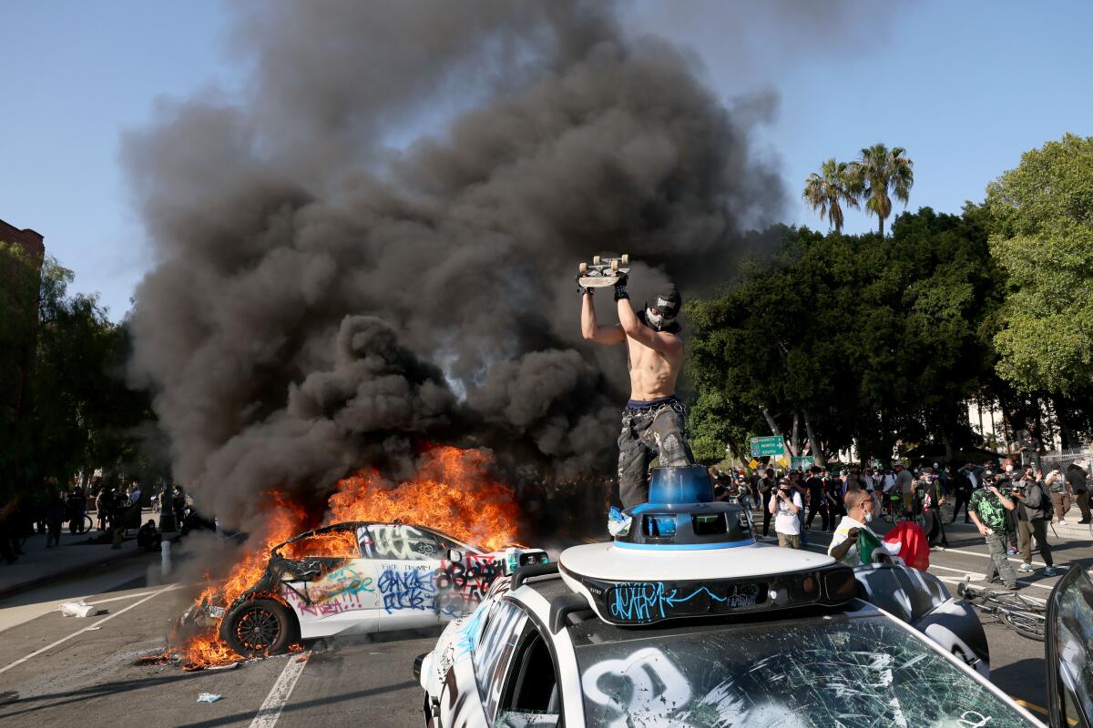 A protester stands atop a white vehicle as another burns behind him