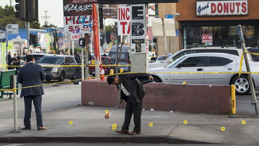 Los Angeles police detectives investigate the scene where three teens were shot, one fatally, in front of a strip mall at 60th Street and Vermont Avenue.