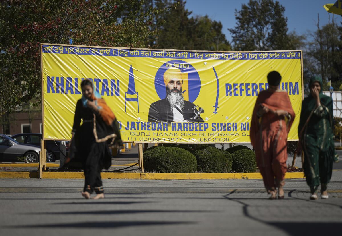 People walking near a large yellow banner picturing a man in a turban and words including "Khalistan Referendum" in blue