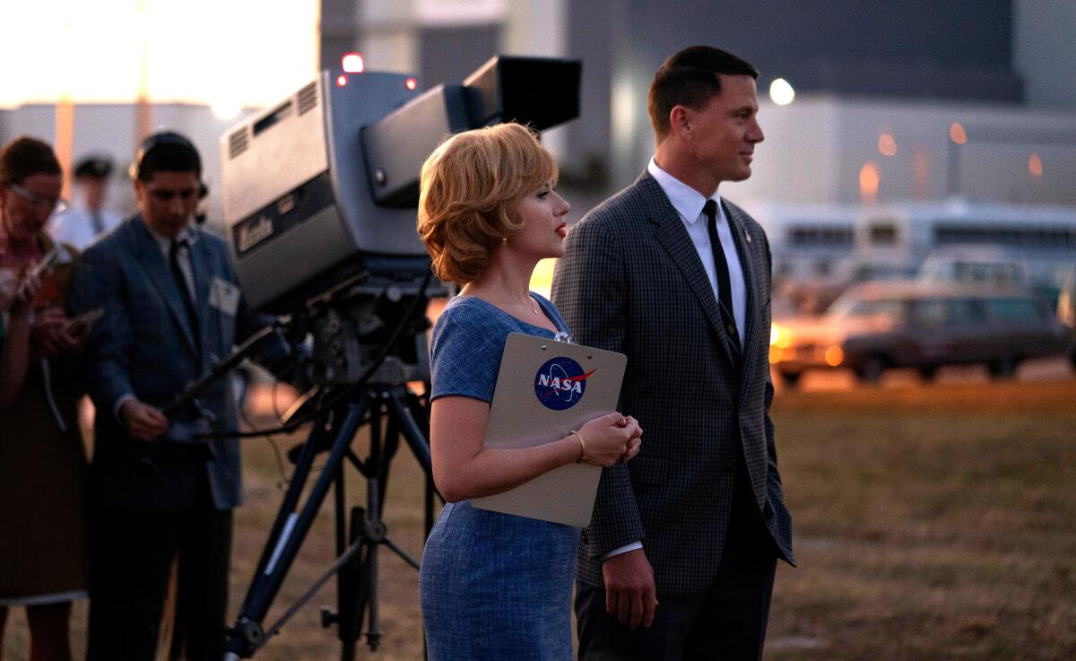 A woman with a NASA clipboard and a man in a suit look off camera.