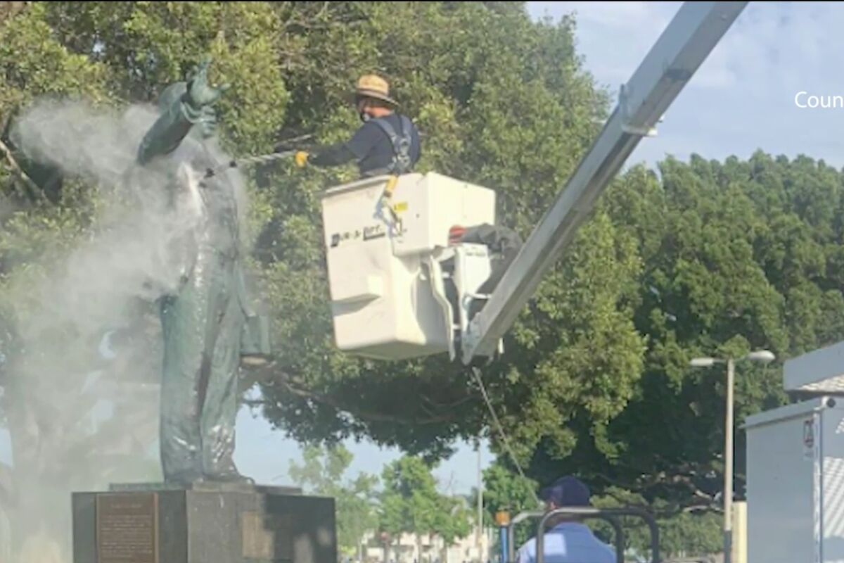 A worker on a crane trains a hose on a statue 