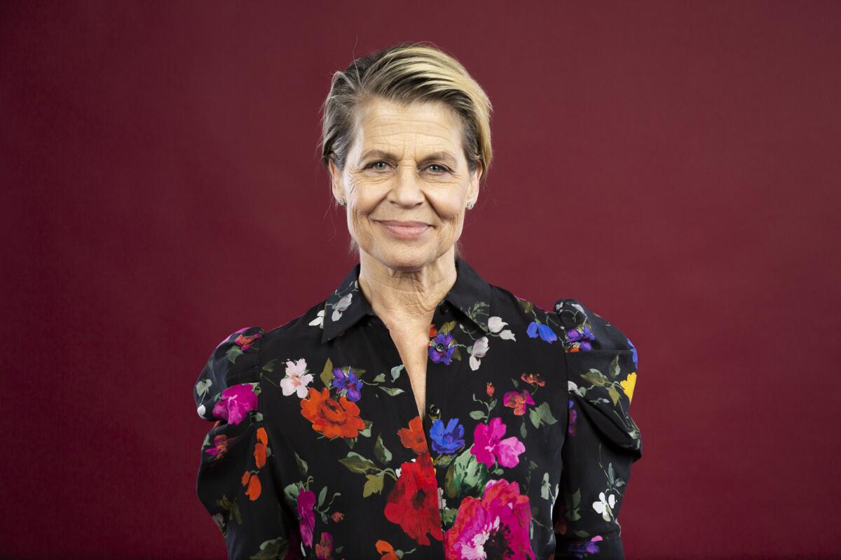 Linda Hamilton poses for a portrait wearing a black, long-sleeved blouse with various flowers of all colors printed on it