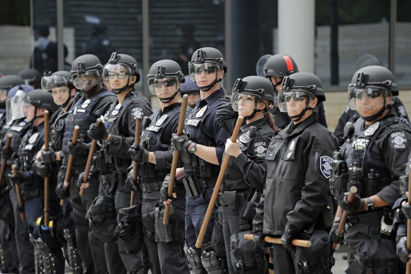 A line of police officers surrounding City Hall on Wednesday, June 3, 2020, in Seattle, look towards demonstrators following protests over the death of George Floyd, an African American who died on May 25 after a white Minneapolis police officer pressed a knee into his neck for several minutes even after he stopped moving and pleading for air. (AP Photo/Elaine Thompson)