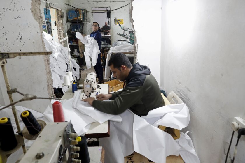 FLE - In this Monday, March 30, 2020 file photo, Palestinians make protective overalls meant to shield people from the coronavirus, to be exported to Israel, at a local factory, in Gaza City. For the first time in years, some sewing factories in the Gaza Strip are back to working at full capacity — producing masks, gloves and protective gowns, some of which are bound for Israel.(AP Photo/Adel Hana, File)