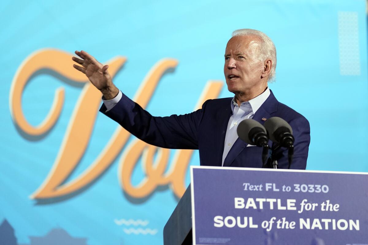 Joe Biden raises his right arm to gesture while he speaks at a lectern.