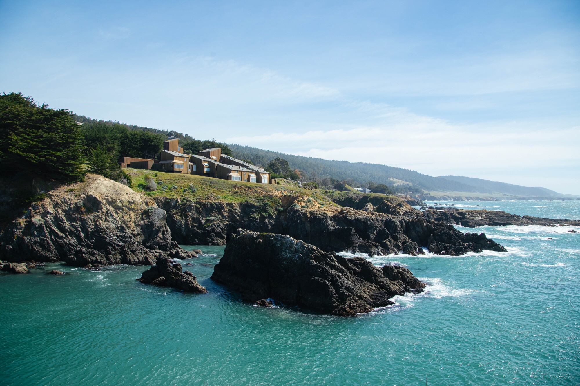 A building on a bluff overlooking a rocky coastline and the Pacific Ocean.