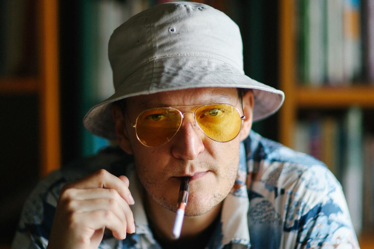 Gabriel Ebert, in yellow aviator sunglasses and a bucket hat with a cigarette in his mouth, as journalist Hunter S. Thompson.