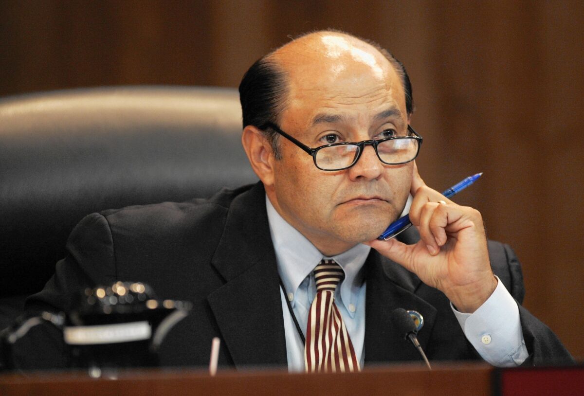 Lou Correa, holding a pen and propping up his chin, listens while sitting in the state Assembly chamber.