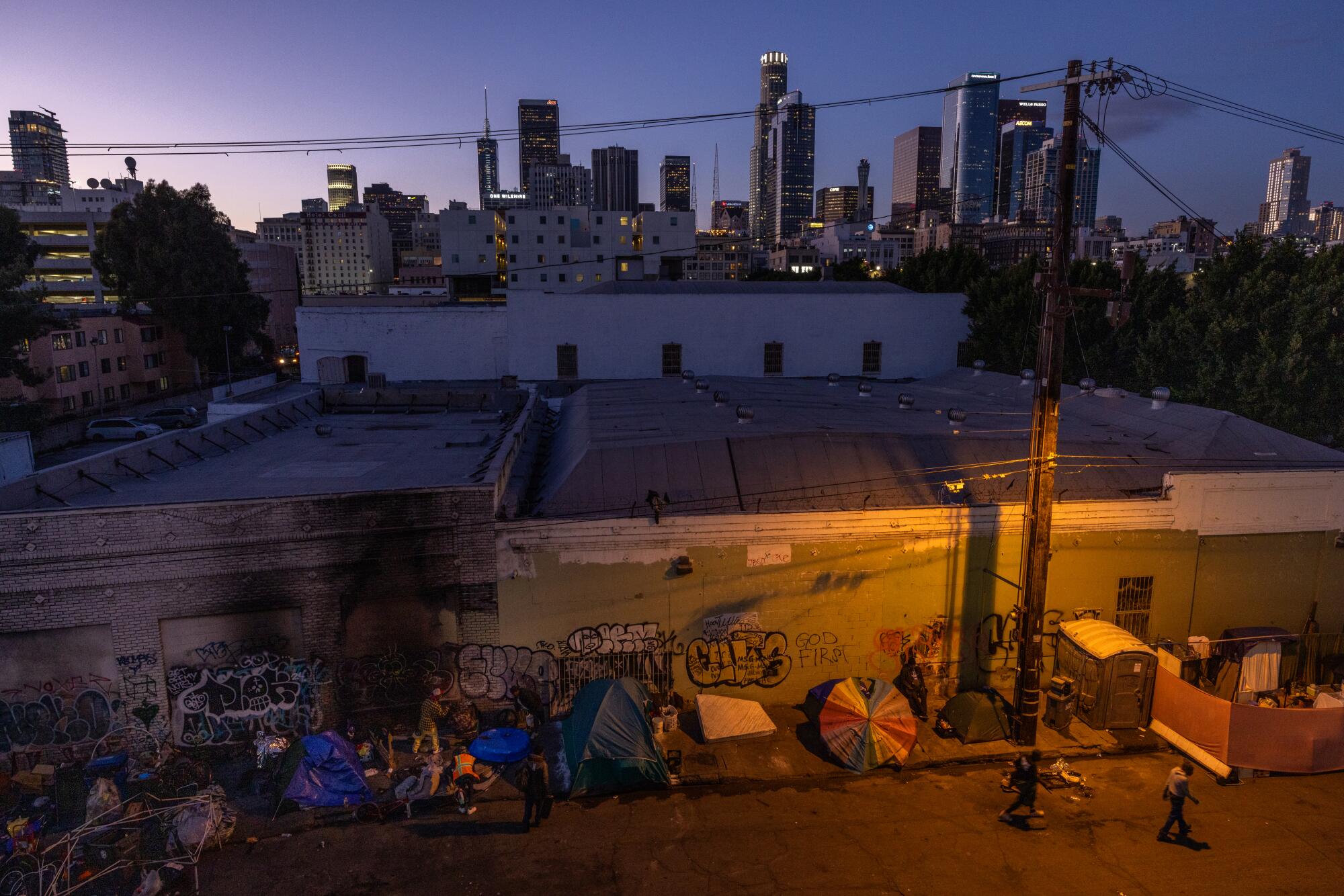 People gather on San Julian Street near 6th Street in the heart of Skid Row with downtown L.A. in the background in 2024.
