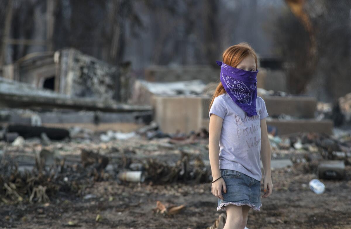 Chloe Hoskins, 7, wearing a bandanna to protect herself from the smoke and ash, checks on a neighbor's burned-out property with her father in the Coffey Park neighborhood in Santa Rosa.