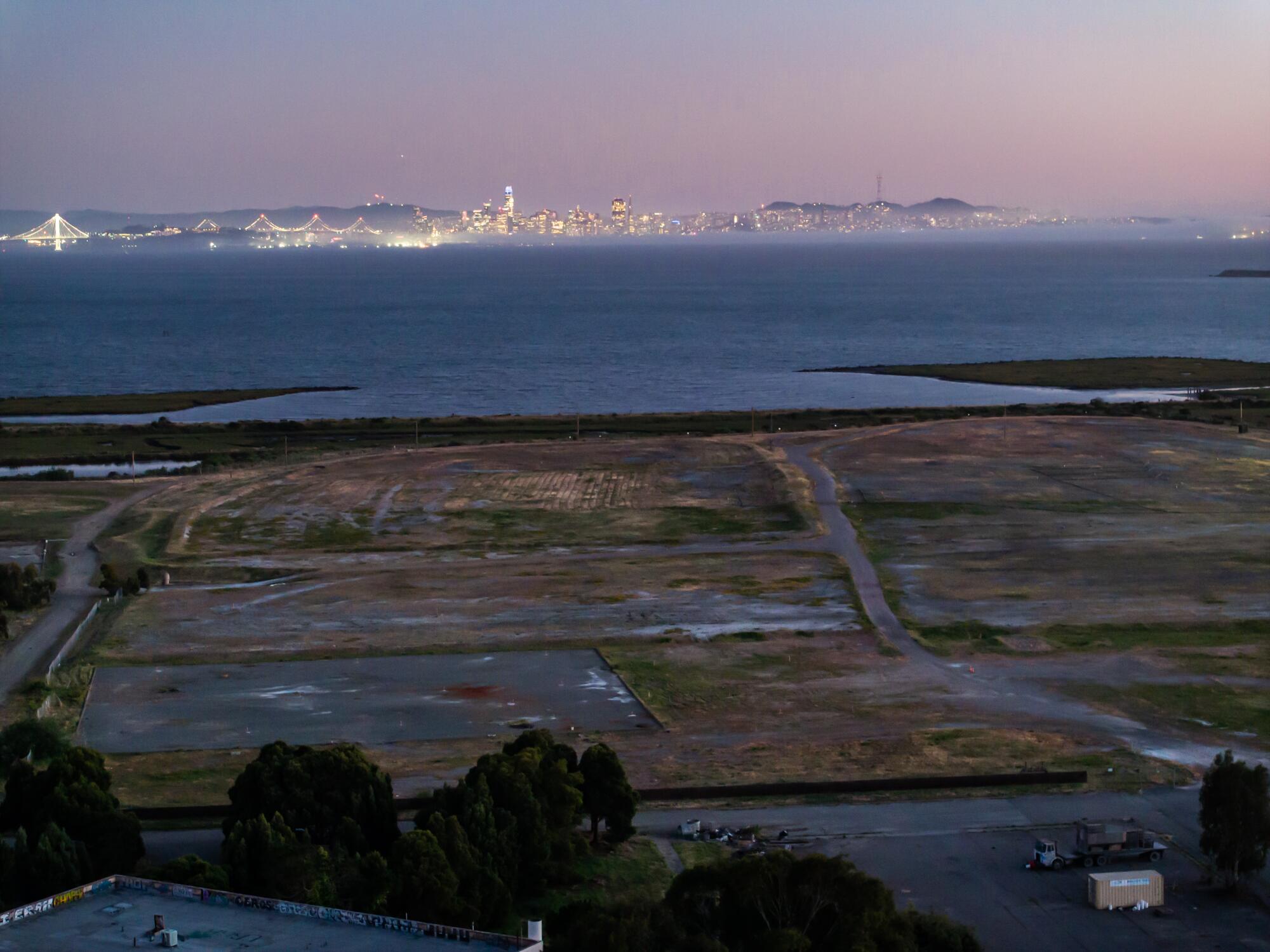 A field is shown, with the lights of San Francisco in the background.
