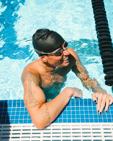 Swimmer Cody Epperson, in a black bathing cap and goggles, perches at the edge of a pool