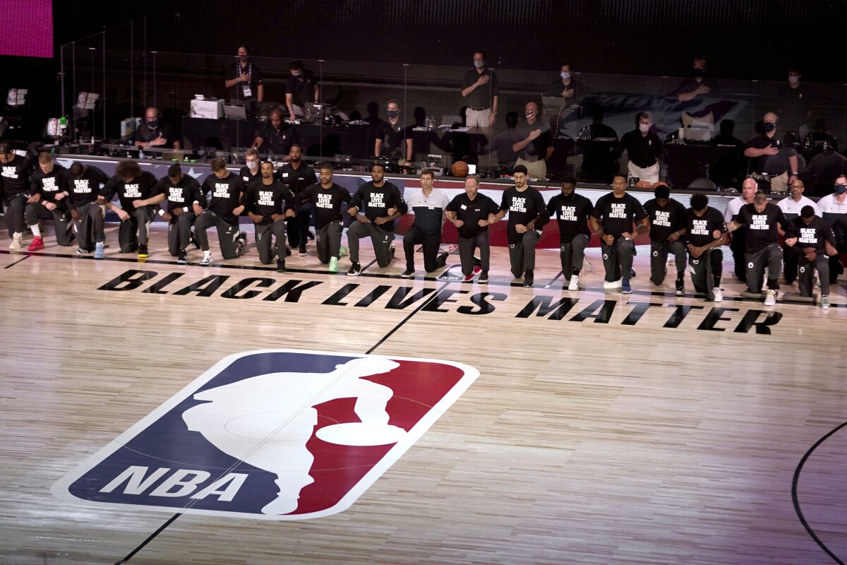 I membri dei Milwaukee Bucks e dei Boston Celtics si inginocchiano attorno al logo Black Lives Matter