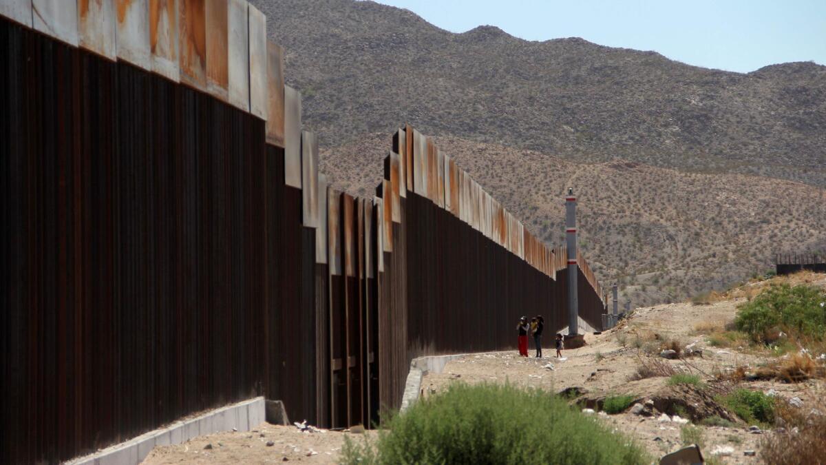 In May, a Mexican family stands next to the border wall between Mexico and the United States, in Ciudad Juarez, Mexico.