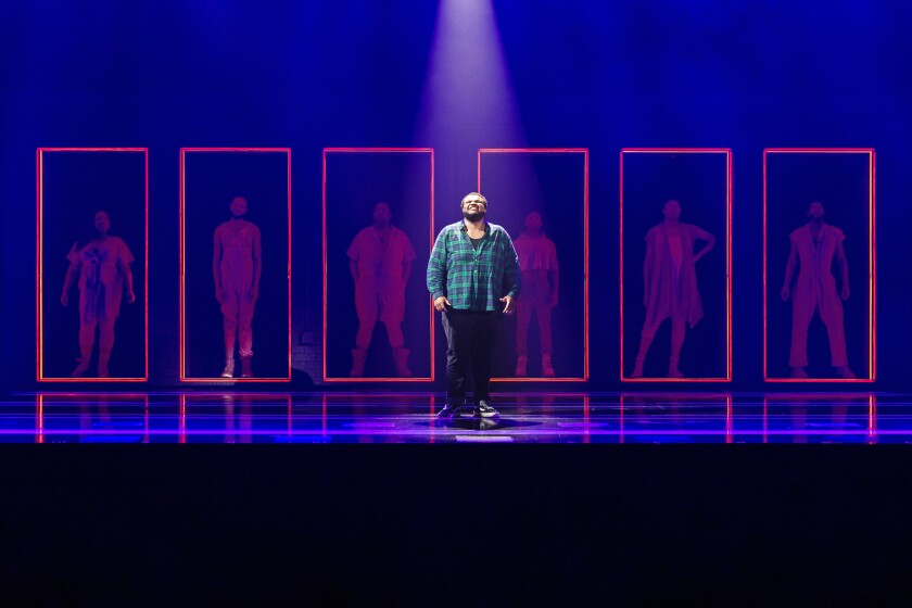 A person stands onstage in front of six other people outlined by pink rectangles.