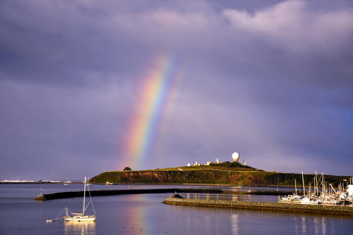 A rainbow arcs through a darkened sky near a bay.