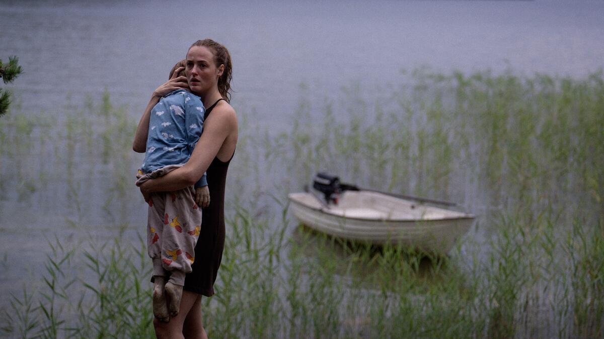 A woman stands in a pond holding her child.