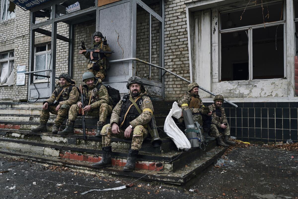 Ukrainian soldiers rest on the steps of a building.