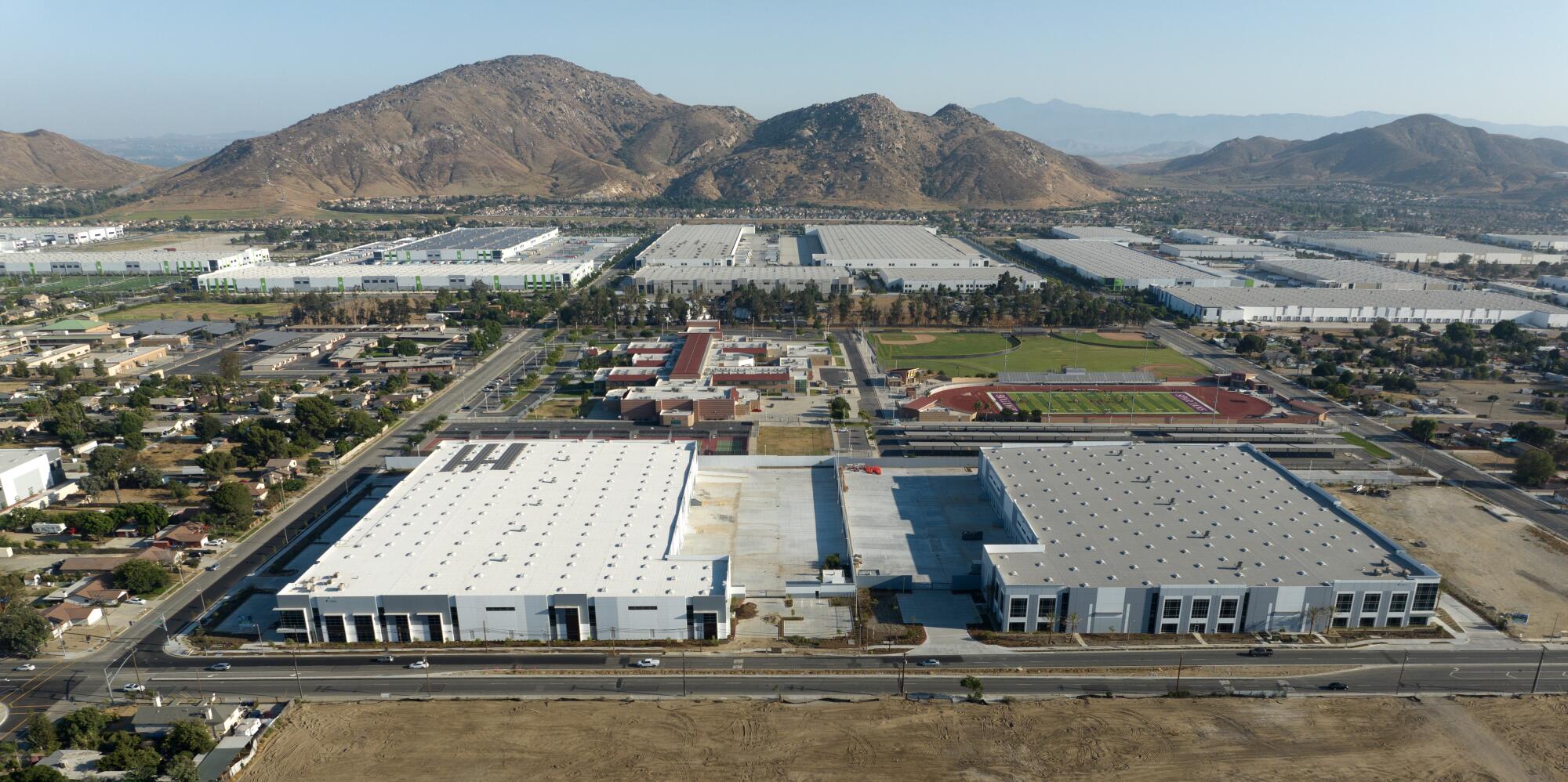 An aerial view of large warehouses with mountains rising in the background.