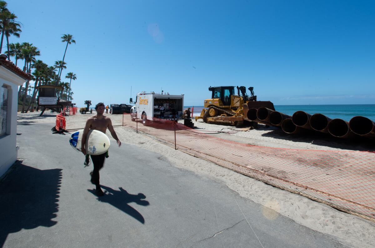 A surfer walks past a construction zone in San Clemente before crews began working on a beach nourishment project.
