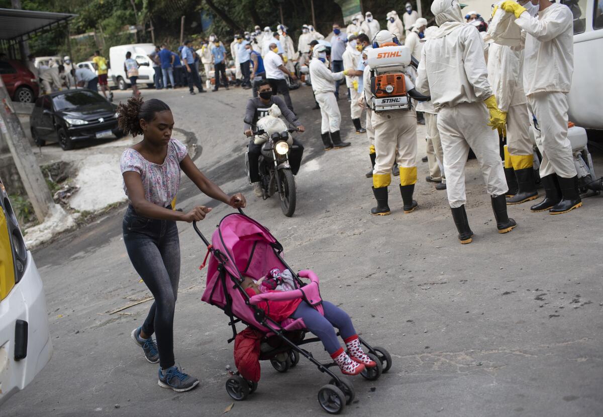 A woman walks past workers who will disinfect the Turano favela in an effort to curb COVID-19's spread  in Rio de Janeiro.