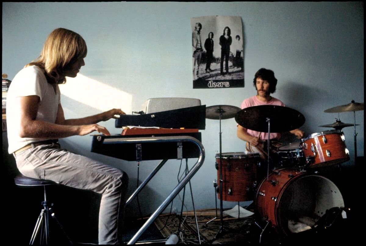 A man playing keyboards and a man playing drums, in a room