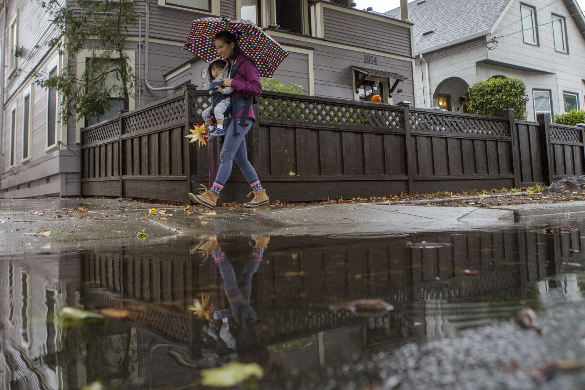 Allison Chan carries son Ian Dimaano as she walks past a puddle as rain falls