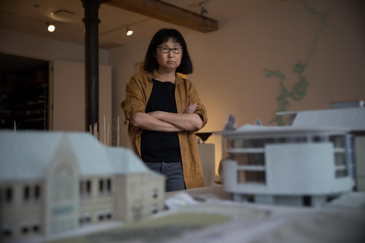 Maya Lin stands, arms crossed, behind a model of Neilson Library in her studio