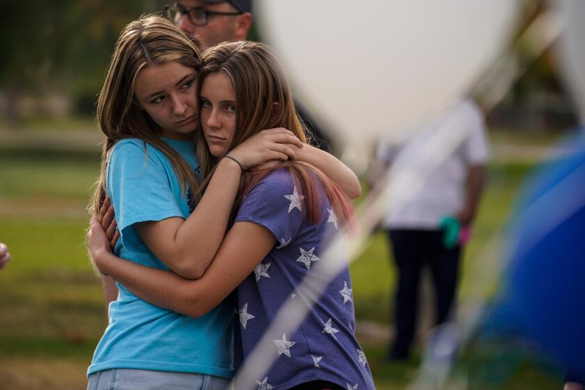 SANTA CLARITA, CALIF. - NOVEMBER 15: Sisters Isabella Esser, 16, and Sophoia Esser, 12, hug, as a memorial grows as people place flowers and pay their respects at Central park on Friday, Nov. 15, 2019 in Santa Clarita, Calif. The school remains closed a day after a shooting where a teenage boy gunned down fellow students on November 14, 2019. (Kent Nishimura / Los Angeles Times)