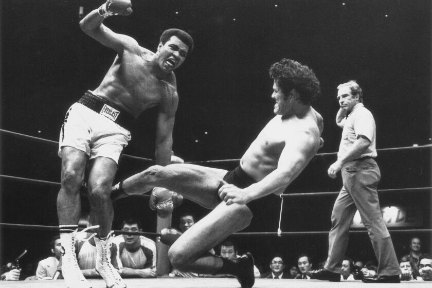 CORRECTS TO 1976, NOT 1979 - FILE - Japanese pro wrestler Antonio Inoki kicks the back of Muhammad Ali's leg during their boxing-wrestling bout at the Budokan hall in Tokyo, June 26, 1976. A popular Japanese professional wrestler and lawmaker Antonio Inoki, who faced a world boxing champion Muhammad Ali in a mixed martial arts match in 1976, has died at 79. The New Japan Pro-Wrestling Co. says Inoki, who was battling an illness, died earlier Saturday, Oct. 1, 2022. (AP Photo, File)