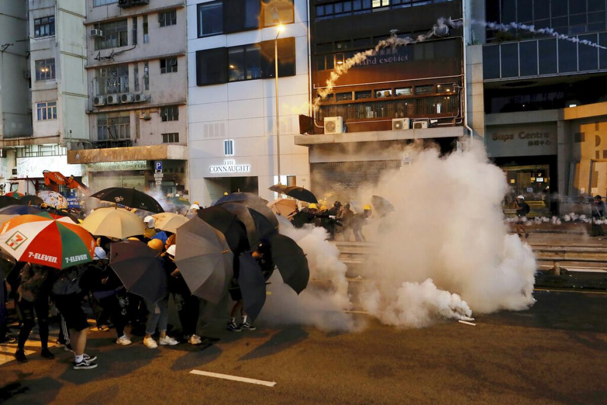 Protesters in Hong Kong use umbrellas to shield themselves from tear gas fired by police as they face off on a street.