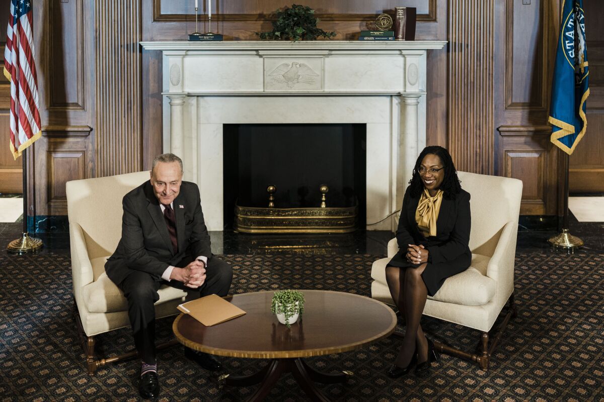 A man and woman sitting with hands clasped in front of an ornate fireplace, with a round coffee table between them