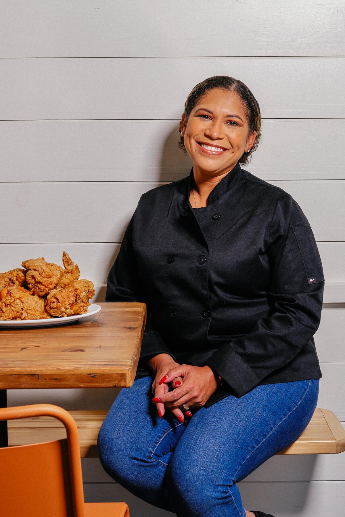 A woman seated at a table next to a plate piled high with fried chicken.