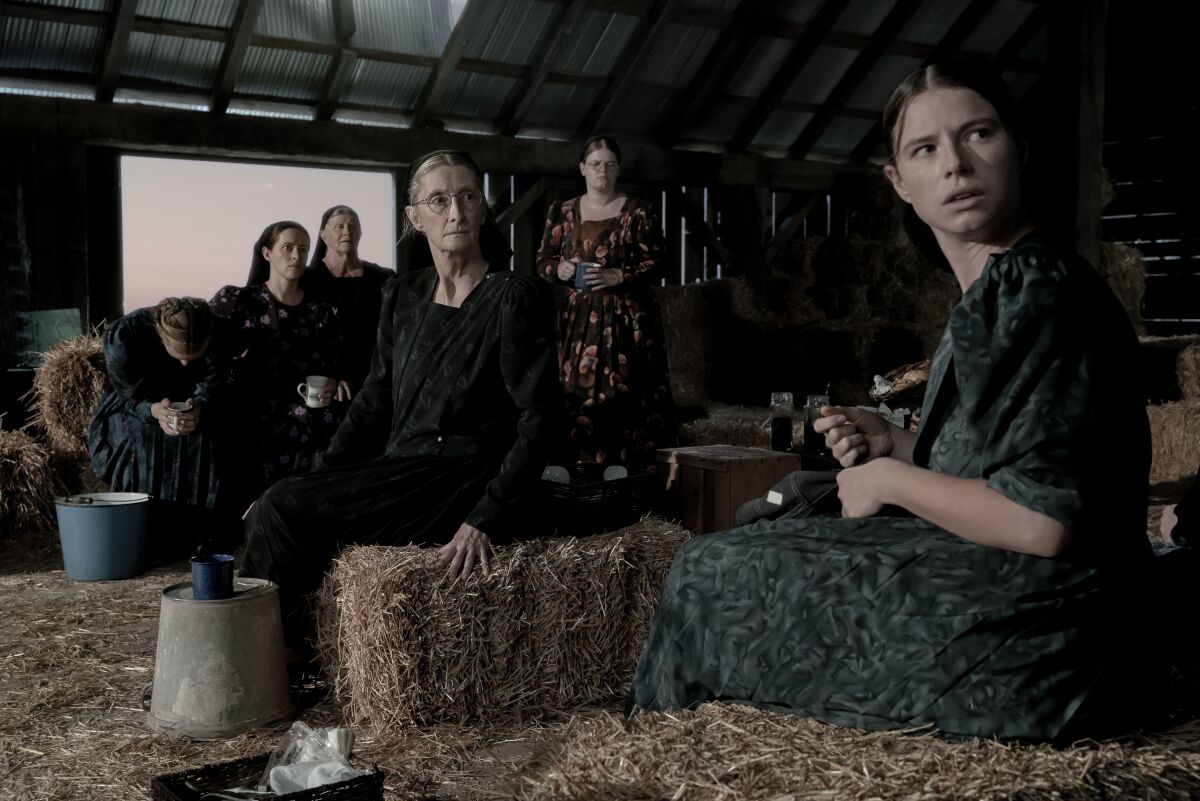 Women in modest dresses and head coverings gather in a hayloft