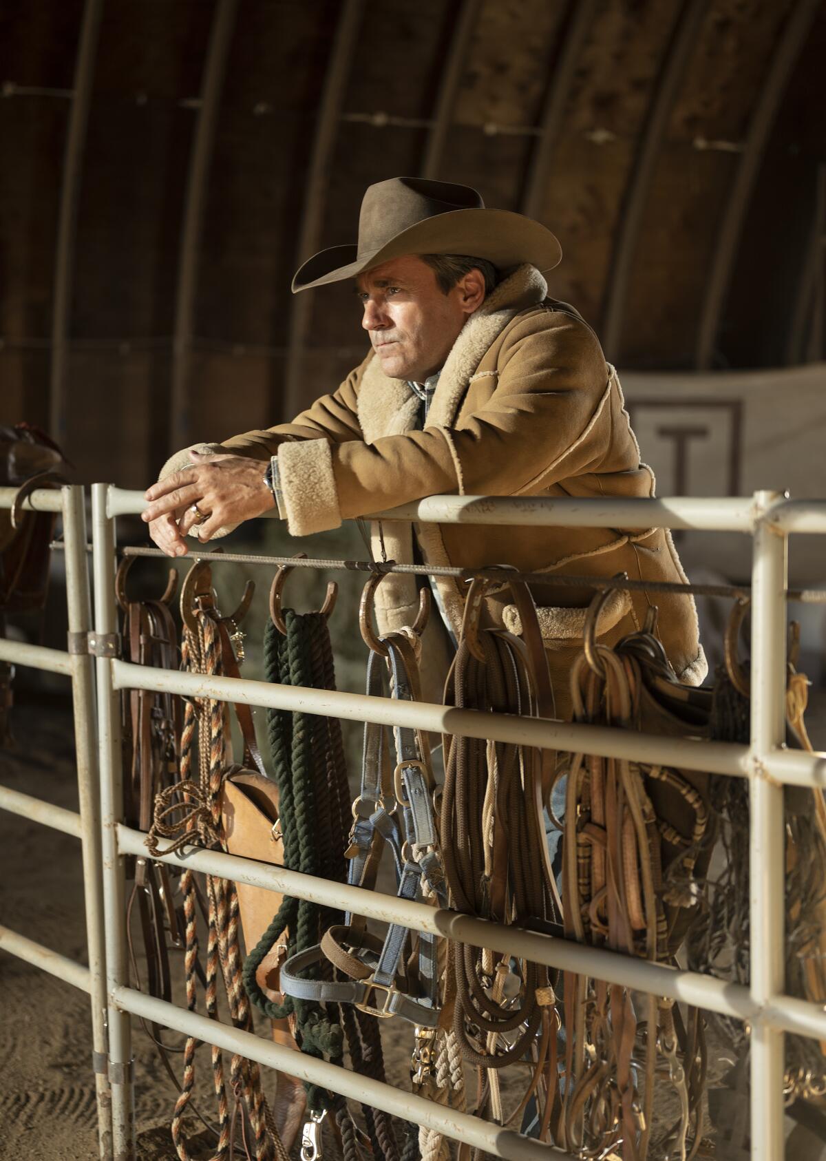 A man in a sherpa coat and Stetson leans against a railing.